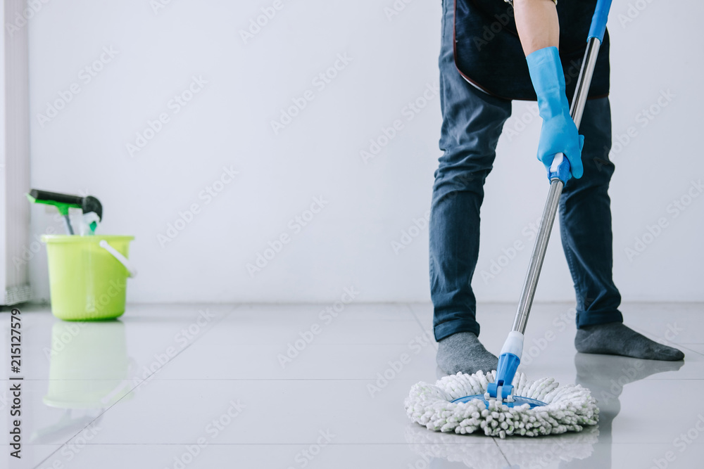 Fototapeta premium Husband housekeeping and cleaning concept, Happy young man in blue rubber gloves wiping dust using mop while cleaning on floor at home