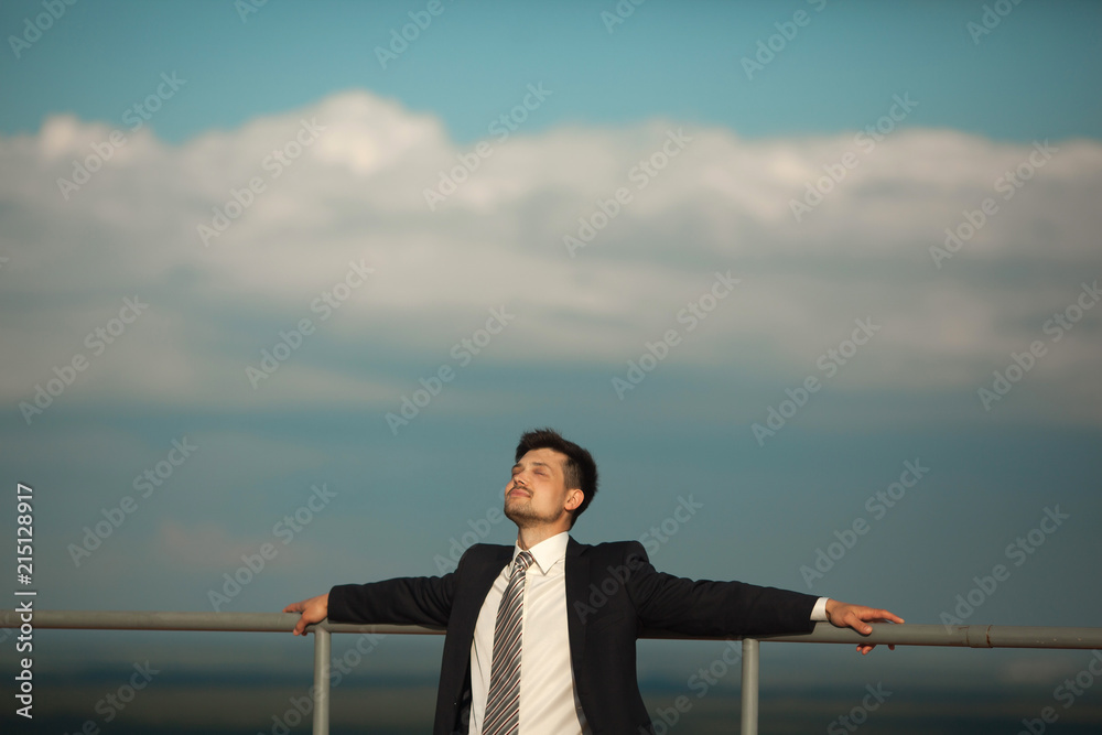 handsome young man in a suit resting with closed eyes against a sky in summer handsome young man in a suit resting with closed eyes against a sky in summer