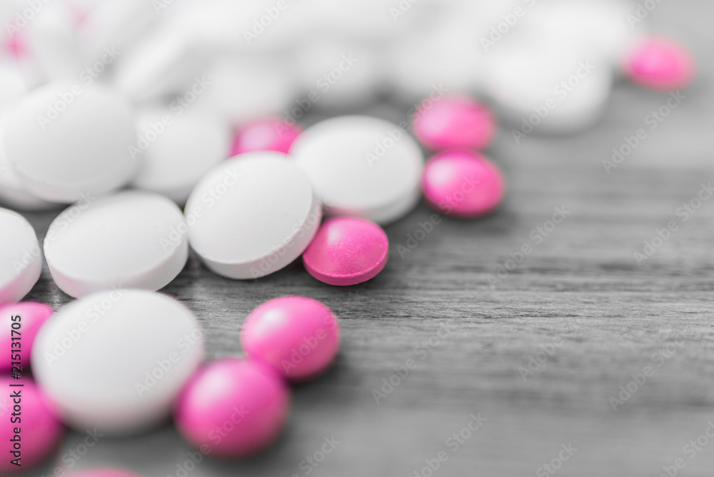 Large white calcium pills and small pink pills close-up on a light wooden background Large white calcium pills and small pink pills close-up on a light wooden background