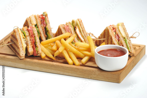 Club-sandwich and french fries on a light wooden board. Next to the potatoes is a cup of ketchup. White background. Close-up. 