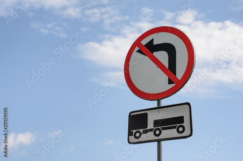 Reflective round road sign that prohibits turning left (No Left Turn sign) and a plate for it indicating that the prohibition applies only to trucks with a trailer, free space on the left, blue sky  photo