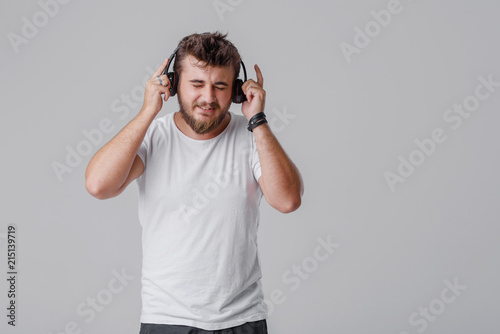 A young man with a beard listens to loud music in wireless headphones. He does not like these sounds