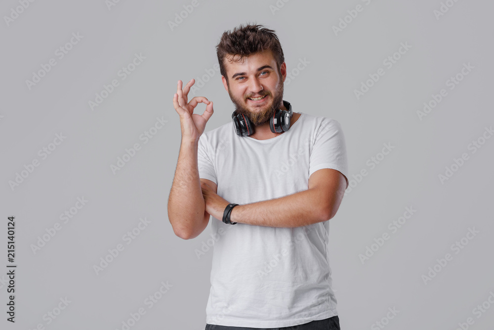 A young man with a beard with wireless headphones around his neck. OK gestures with his fingers, everything is fine. He likes music A young man with a beard with wireless headphones around his neck. OK gestures with his fingers, everything is fine. He likes music