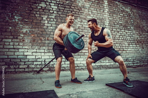 Two muscular athletes training, one raise the bar when other is motivating. Scream. Working hard. Street gym. Exercise for the muscles of the back