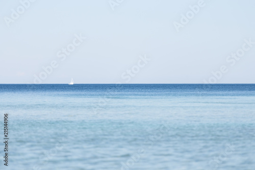 A white sailboat on the horizon of a body of water with blue skies