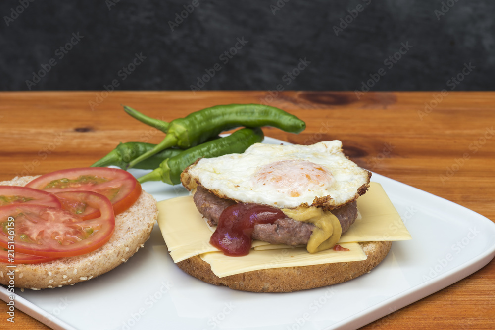 Hamburguesa con queso y huevo, acompañada de rodajas de tomate y pimientos picantes, preparada en casa Hamburguesa con queso y huevo, acompañada de rodajas de tomate y pimientos picantes, preparada en casa