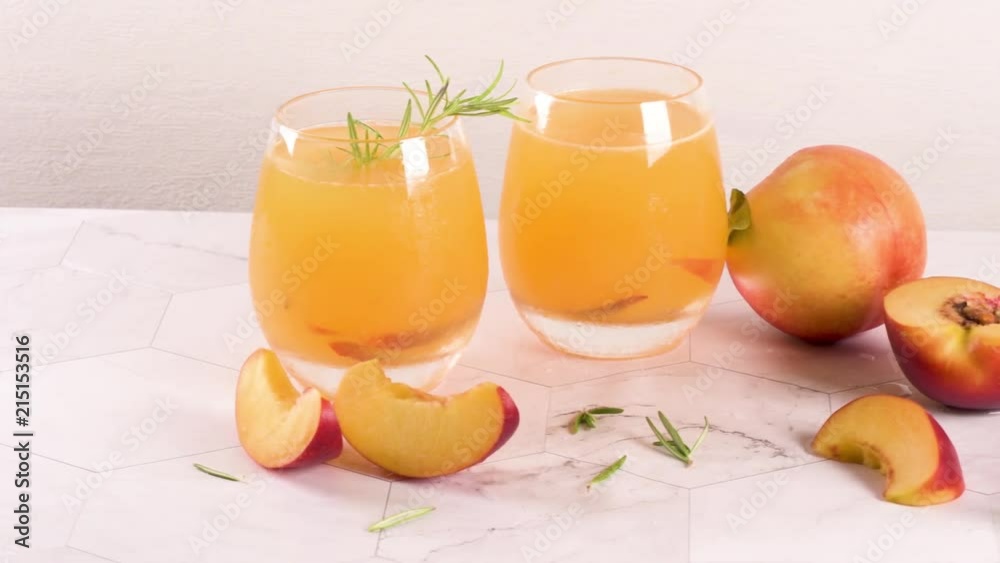 Homemade peach juice with ice cubes and rosemary leaves in glass on marble stone background. Homemade peach juice with ice cubes and rosemary leaves in glass on marble stone background.