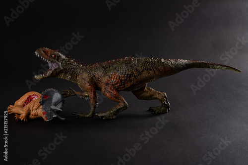Carcharodontosaurus with a triceratops body nearby on dark background close up