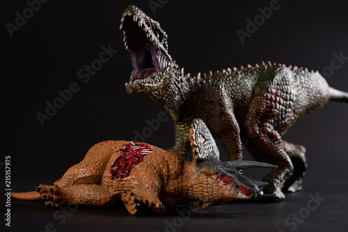 Carcharodontosaurus with a triceratops body nearby on dark background close up photo