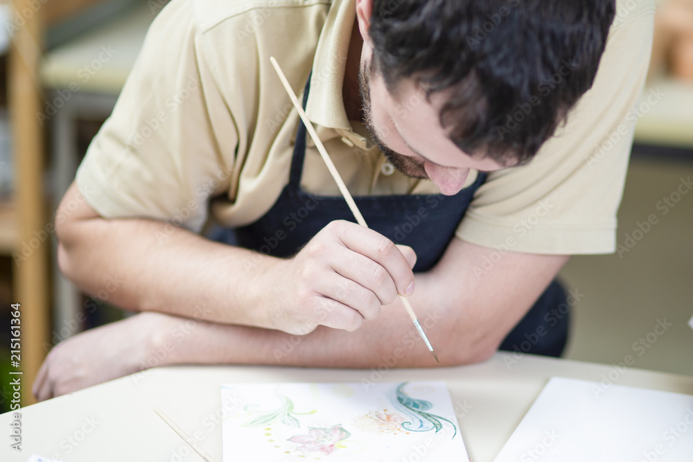 Male Ceramist Using Paintbrush For Glazing and Painting Ceramic Crafts in Studio. Male Ceramist Using Paintbrush For Glazing and Painting Ceramic Crafts in Studio.
