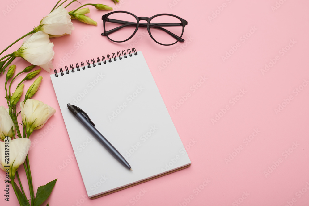 Feminine workplace with jotter, eyeglasses and flowers in pastel Feminine workplace with jotter, eyeglasses and flowers in pastel