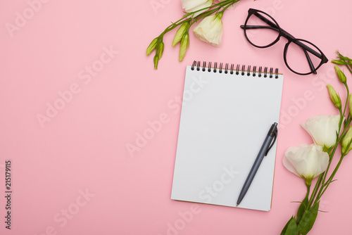 Blank note pad with eyeglasses and flowers on pink background