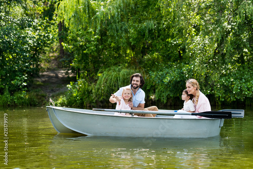 young family spending time together in boat on river at park and looking away