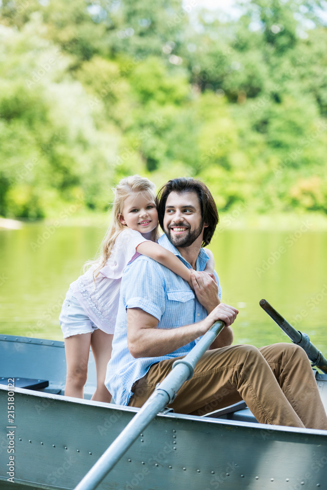 smiling daughter embracing father from behind while they riding boat on lake at park