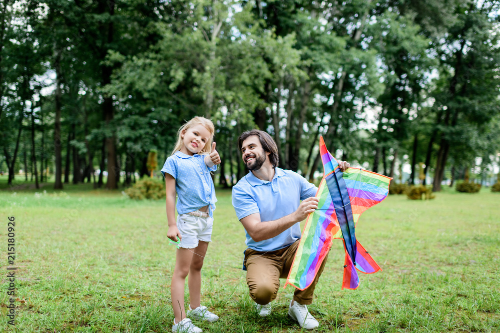 handsome happy father with kite and adorable little daughter spending time together at park