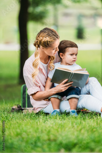 mother and son sitting with book on grass at park