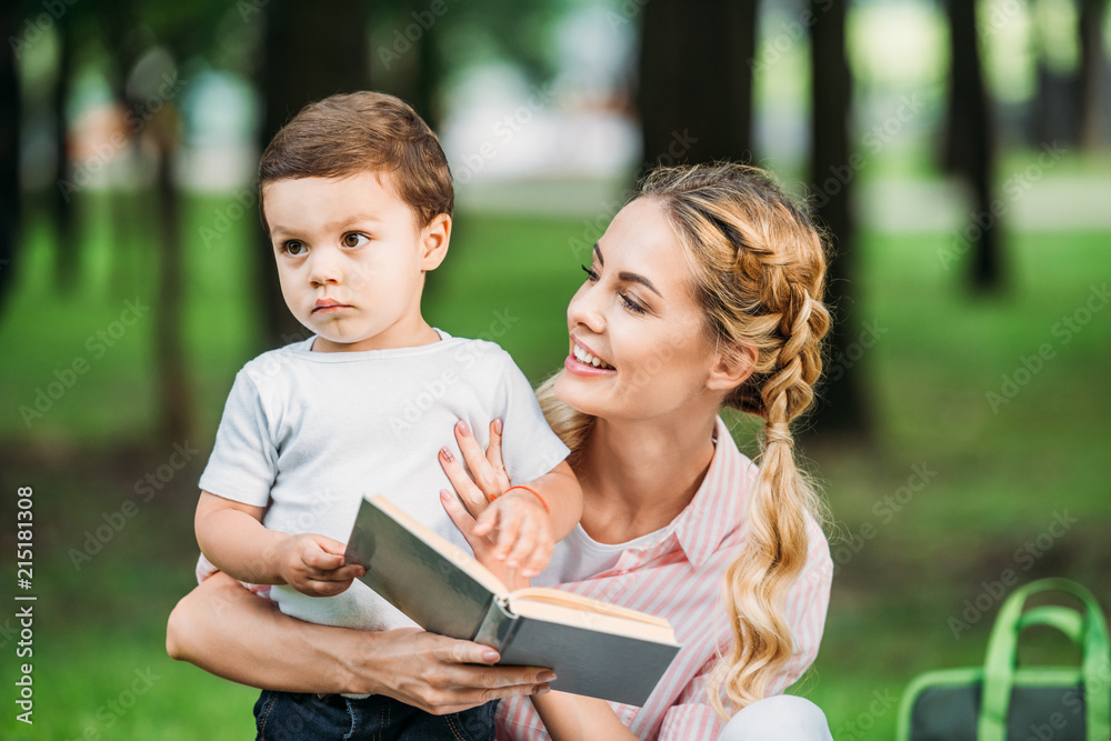 happy mother with sad little son reading book at park happy mother with sad little son reading book at park
