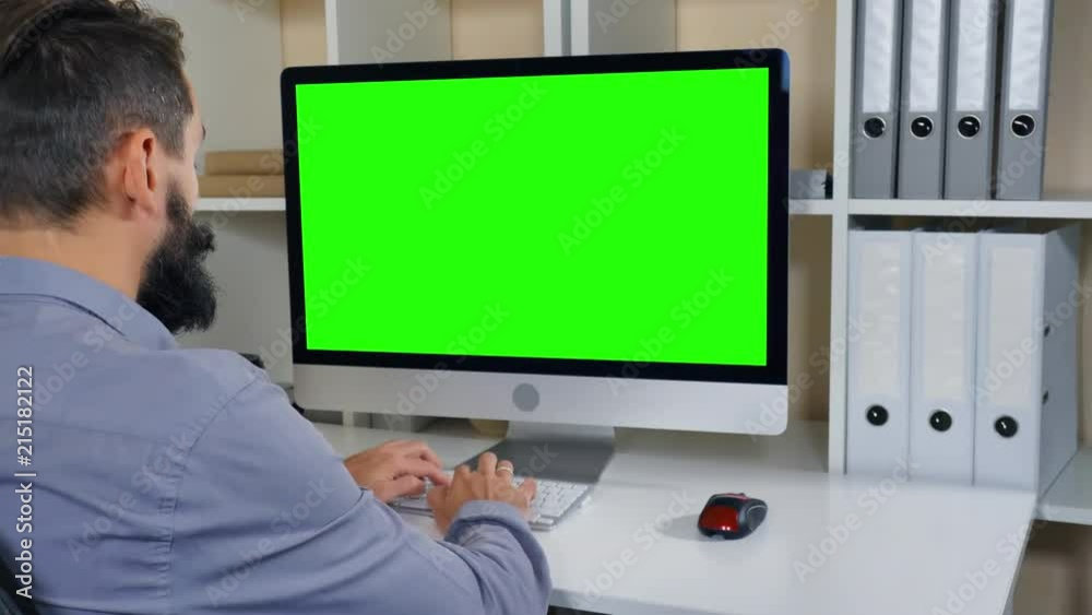 businessman sitting at workplace in small office. man with beard looking on display computer with green screen. employee in startup company typing on keyboard businessman sitting at workplace in small office. man with beard looking on display computer with green screen. employee in startup company typing on keyboard