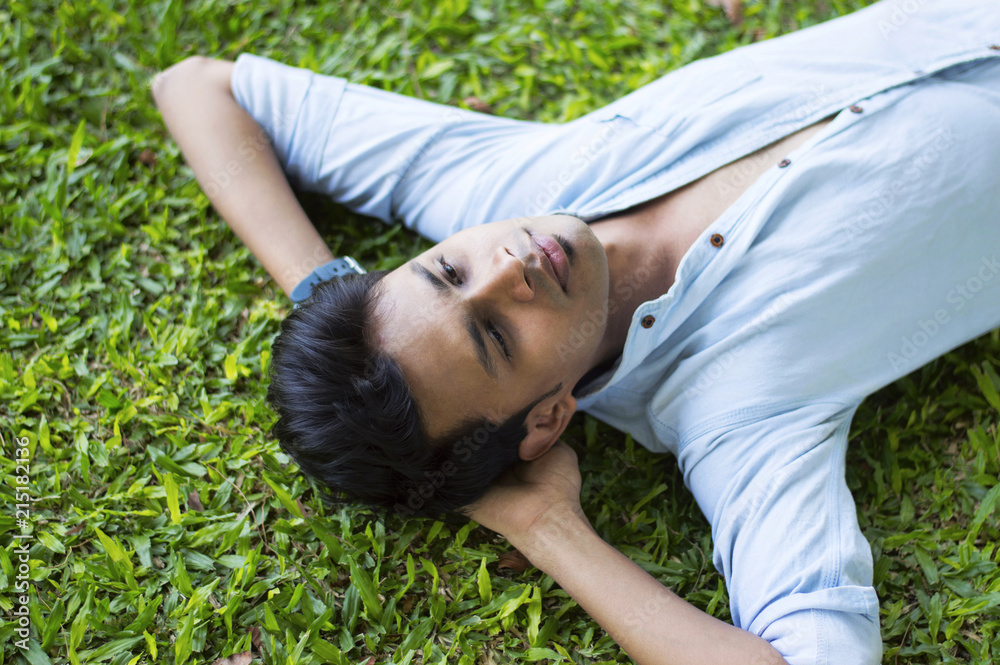 Happy young man lying on the grass relaxing Happy young man lying on the grass relaxing
