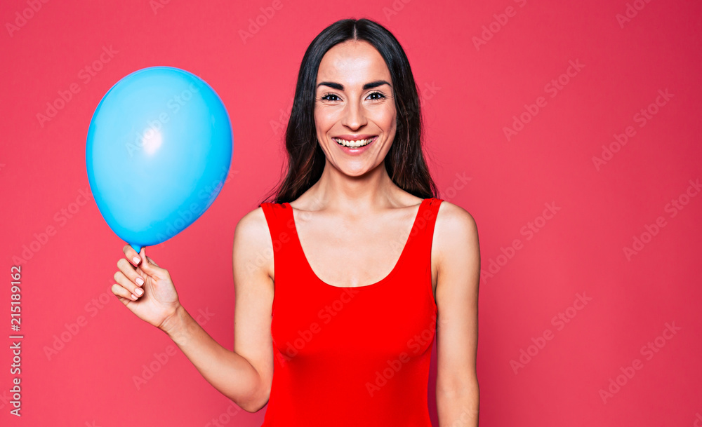 Gorgeous young smiling woman with blue balloon in hand, girl looks on camera over pink background Gorgeous young smiling woman with blue balloon in hand, girl looks on camera over pink background