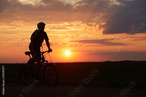 Silhouette of a bicyclist traveling on a sunset background on the road to the field © Sergei Malkov