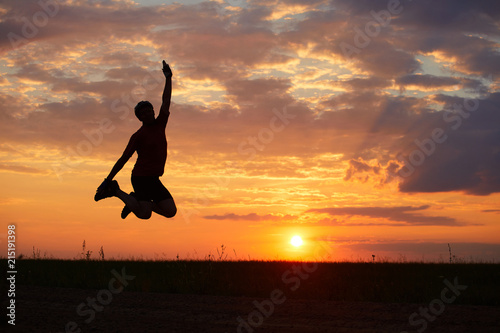 Silhouette of a young man jumping against the sunset with a sense of joy of happiness and freedom
