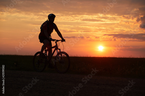 Silhouette of a bicyclist traveling on a sunset background on the road to the field