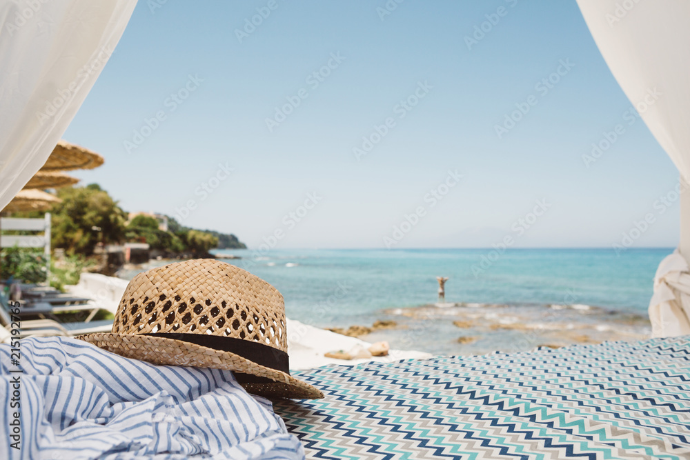Obraz premium Straw hat lying on the beach bed with beauty view to blue the ionian sea, clear sky and girl in water on Greek island Zakynthos in landscape orientation