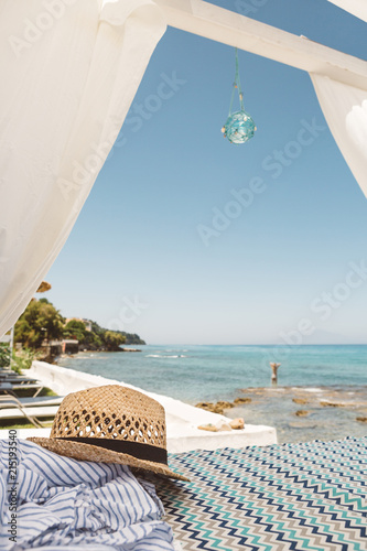 Straw hat on beach bed with view of Ionian Sea and girl in water, Zakynthos, Greece