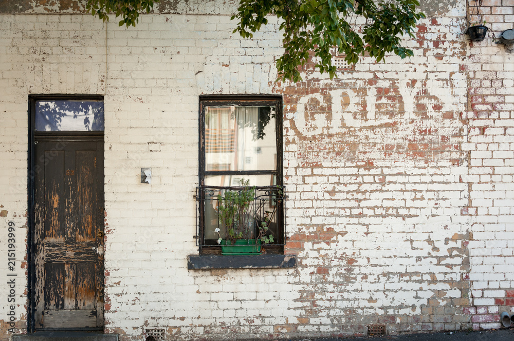the remains of and old painted sign on the side of a building with a brown wooden door and window with planter box