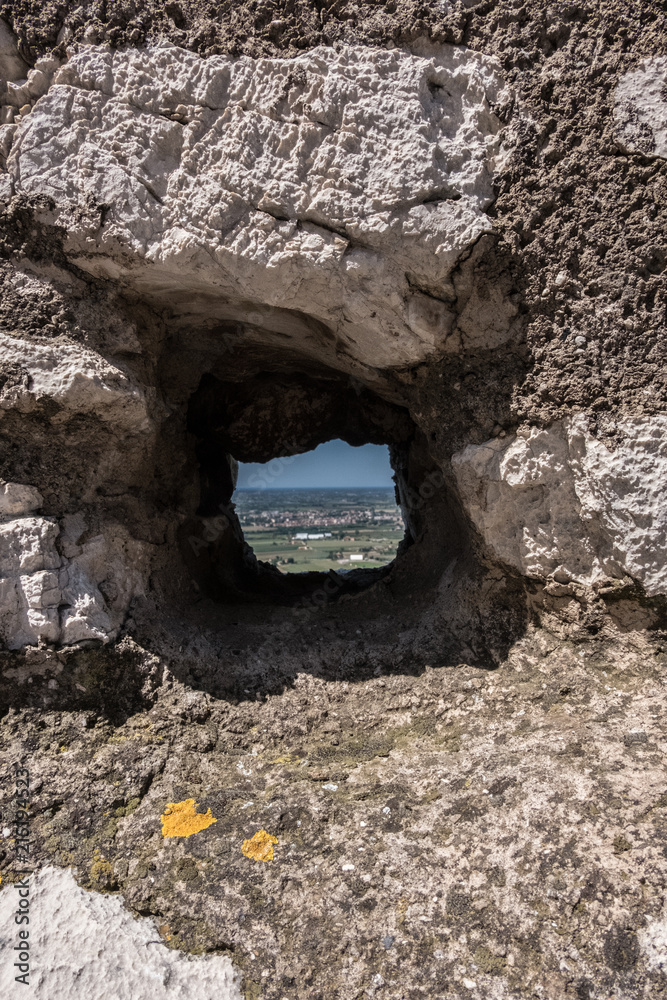 Square hole in an ancient stone wall with landscape view on the background. No people.