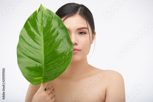 Young Asian woman with big green leaf closing face on white background