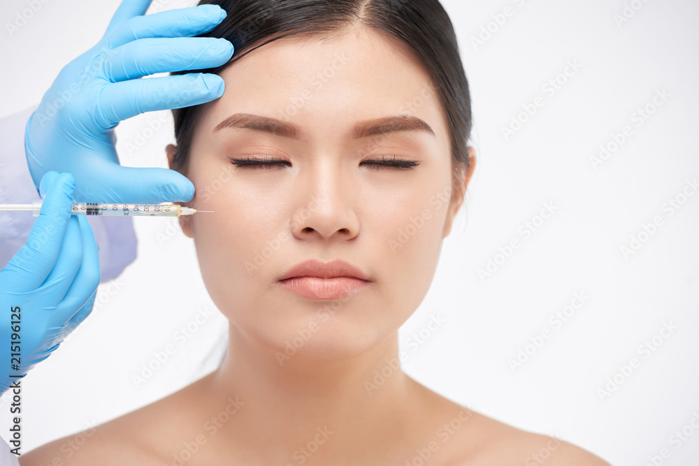 Crop hands in rubber gloves making beauty treatment with syringe to Asian woman with eyes closed