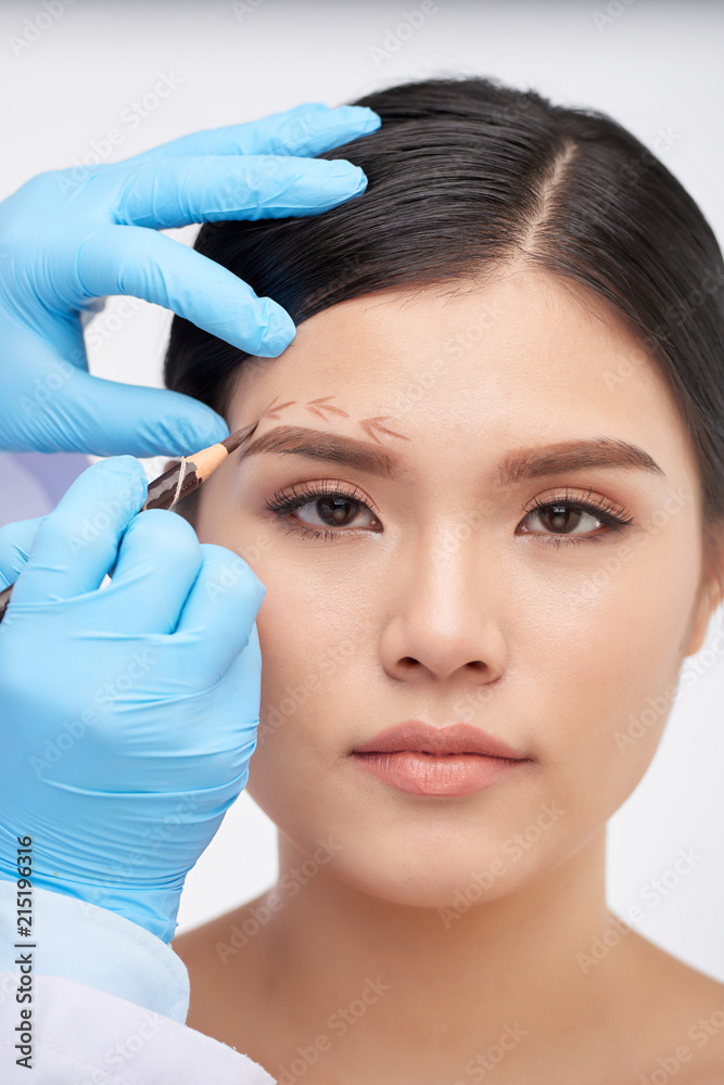 Crop hands in rubber gloves drawing arrows on face of attractive woman on white background