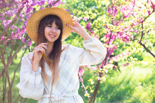 Portrait of young woman in the flowered field in the spring time. Girl wearing white dress and straw sun hat.Copy space.