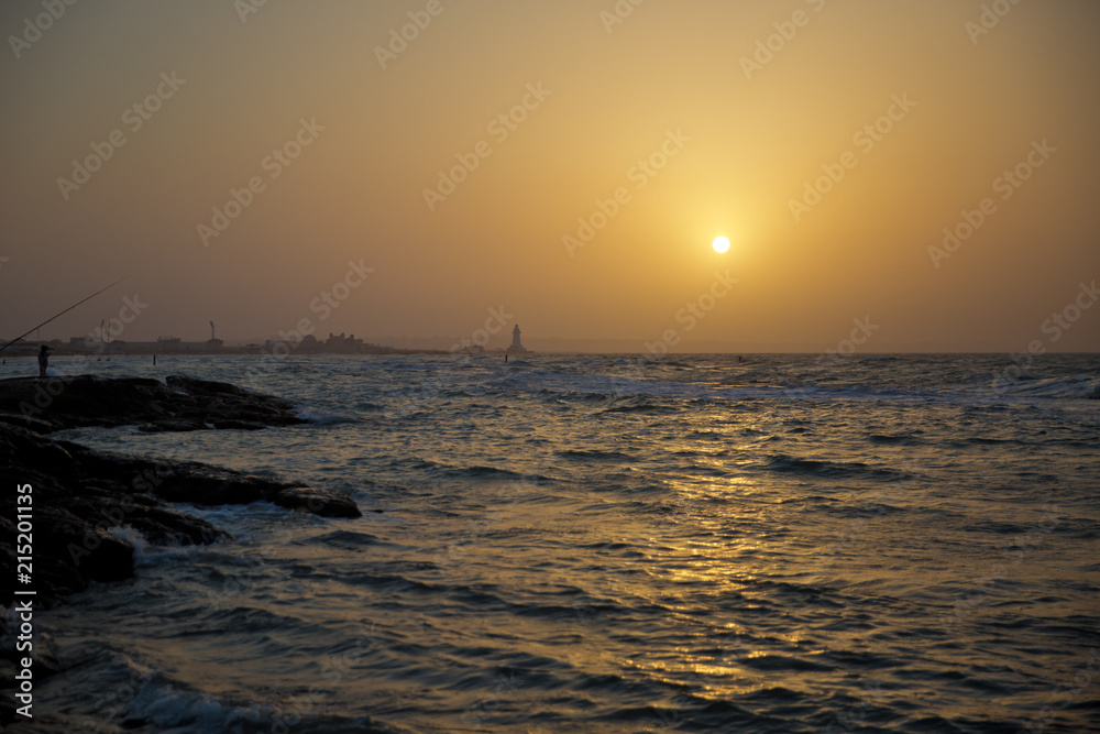 Obraz premium Beautiful sunset at the beach, amazing colors, light beam shining through the cloudscape. Azerbaijan sea and beach . The sound of the sea waves is coming . The fisherman fishes in the sea .