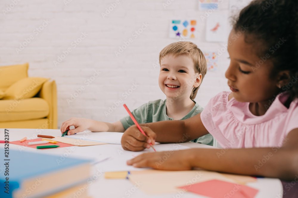 selective focus of multicultural preschoolers at table with papers and pencils in classroom selective focus of multicultural preschoolers at table with papers and pencils in classroom