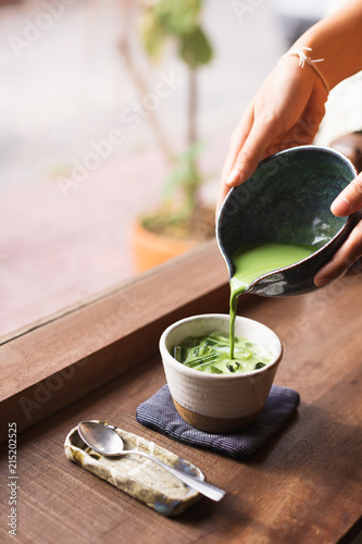 The hand of a woman pouring iced matcha latte near the window in a cafe.