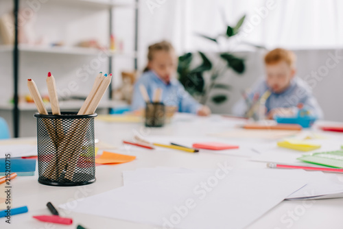 selective focus of adorable kids drawing pictures at table in classroom