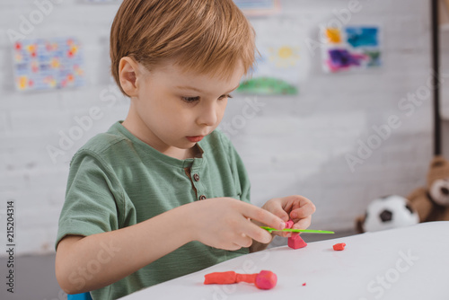 focused boy with colorful plasticine sculpturing figure at table in room photo