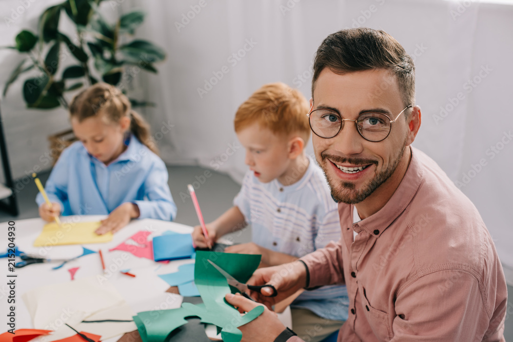 selective focus of smiling teacher and preschoolers making paper applique in classroom selective focus of smiling teacher and preschoolers making paper applique in classroom