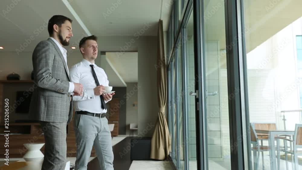 Two businessmen talking standing at the panoramic window with Cup of coffee Two businessmen talking standing at the panoramic window with Cup of coffee