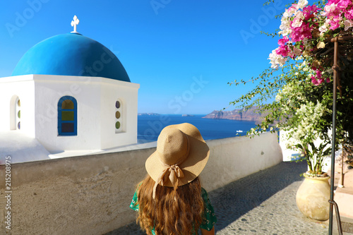 Fotografie Santorini woman walking in beautiful street of Oia village with flowers and typi