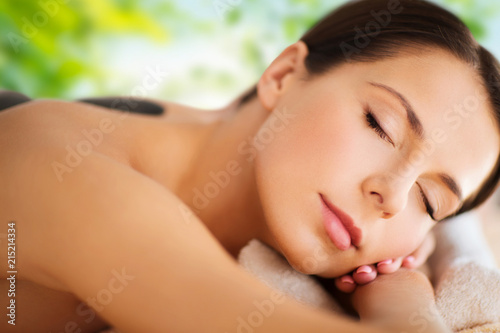 wellness  spa and beauty concept - close up of beautiful woman having hot stone therapy over green natural background