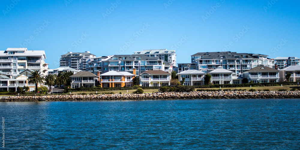 Australian waterside houses and condominiums with rock sea wall against blue sky 