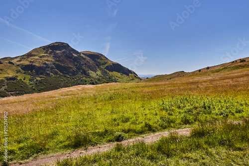 Summer view of Arthur's Seat in Holyrood Park with beautiful green grass and blue sky in Edinburgh, Scotland, United Kingdom.
