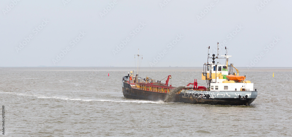 Sand dredging boat drawing away from coast shoreline to pump sand
