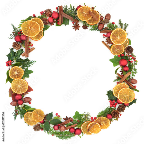 Christmas wreath garland with dried fruit, spice, red bauble decorations, natural winter leaf sprigs, holly berries, acorns and pine cones on white background. Christmas card for the festive season.