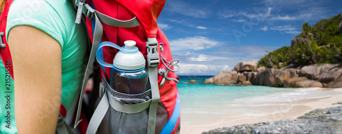 travel, tourism, hike and people concept - close up of woman with water bottle in backpack pocket over background of seychelles island beach in indian ocean