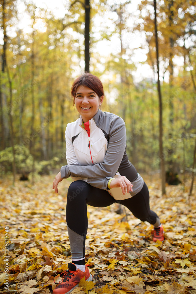 Fototapeta premium Autumn photo of sporty woman stretching in forest at morning against background of trees